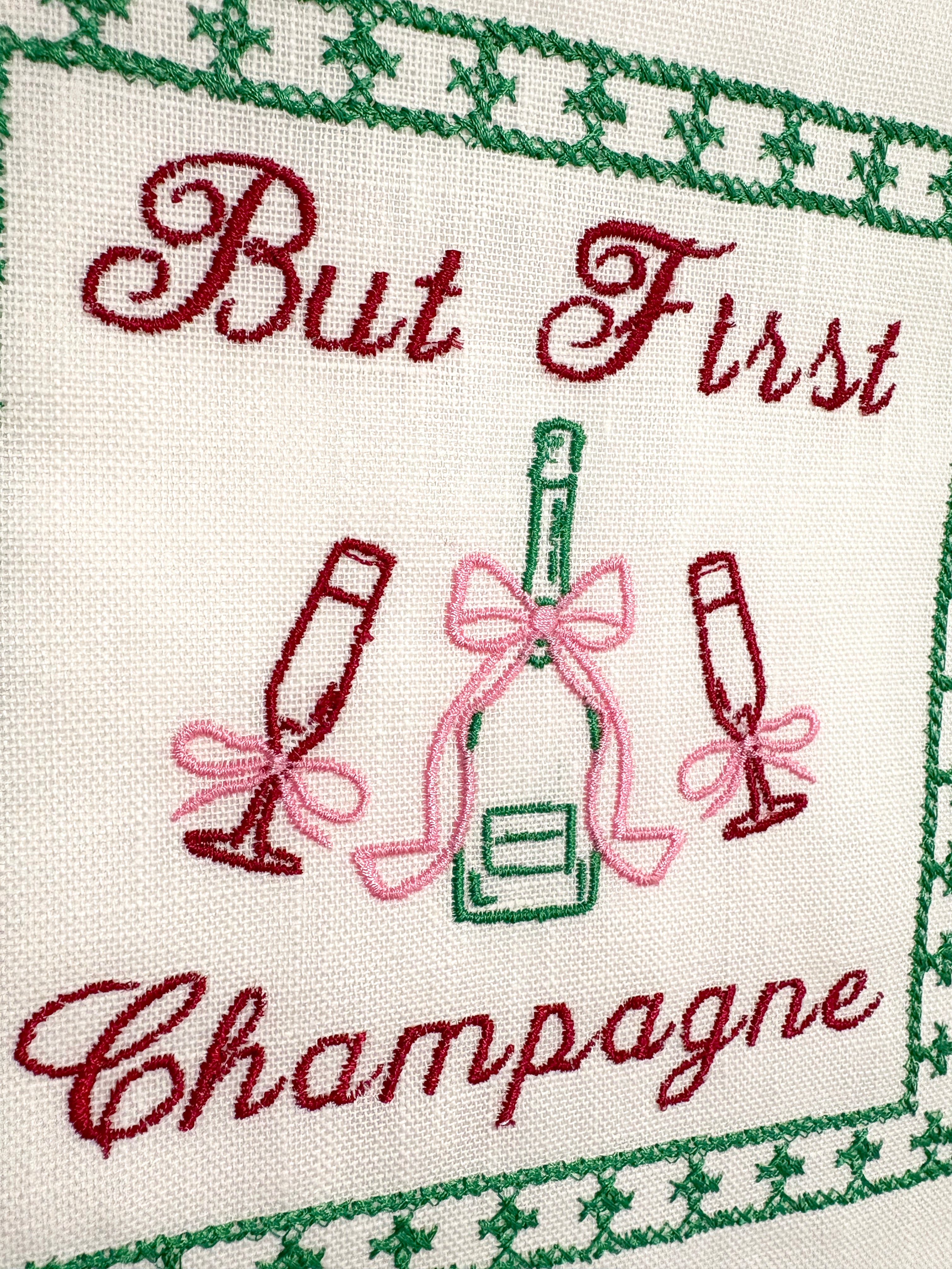 Lillyloves embroidered artwork featuring the phrase "But First Champagne" with decorative floral accents on fabric.