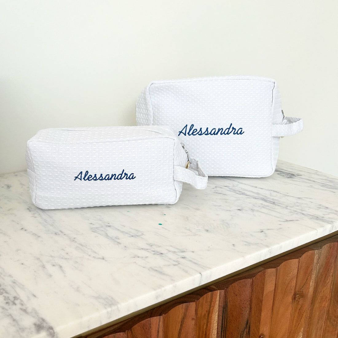 Two Lilly Loves monogram quilted cosmetic wash bags with zipper closures, featuring elegant designs and compact storage.